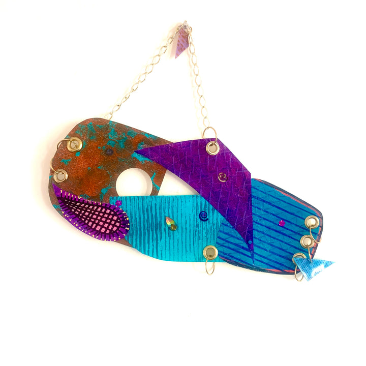 The artwork 'Swinging' features an abstract composition with vibrant turquoise, purple, and rust-colored geometric shapes arranged in a flowing design. The acrylic on paper piece showcases textured patterns including dotted details and linear striations, suspended by a delicate gold chain. 16x18 inches artwork by Sunny Chapman.