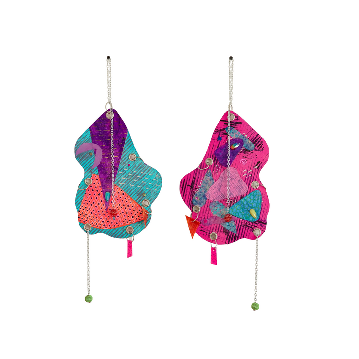 The artwork 'The Day the World Turned Glitter' by Sunny Chapman features vibrant abstract wall hangings in turquoise, purple, and hot pink, adorned with metallic chains and green bead accents. Each piece showcases layered organic shapes with mixed media elements, including glitter, sequins, and jewels, creating a dynamic, dimensional composition.