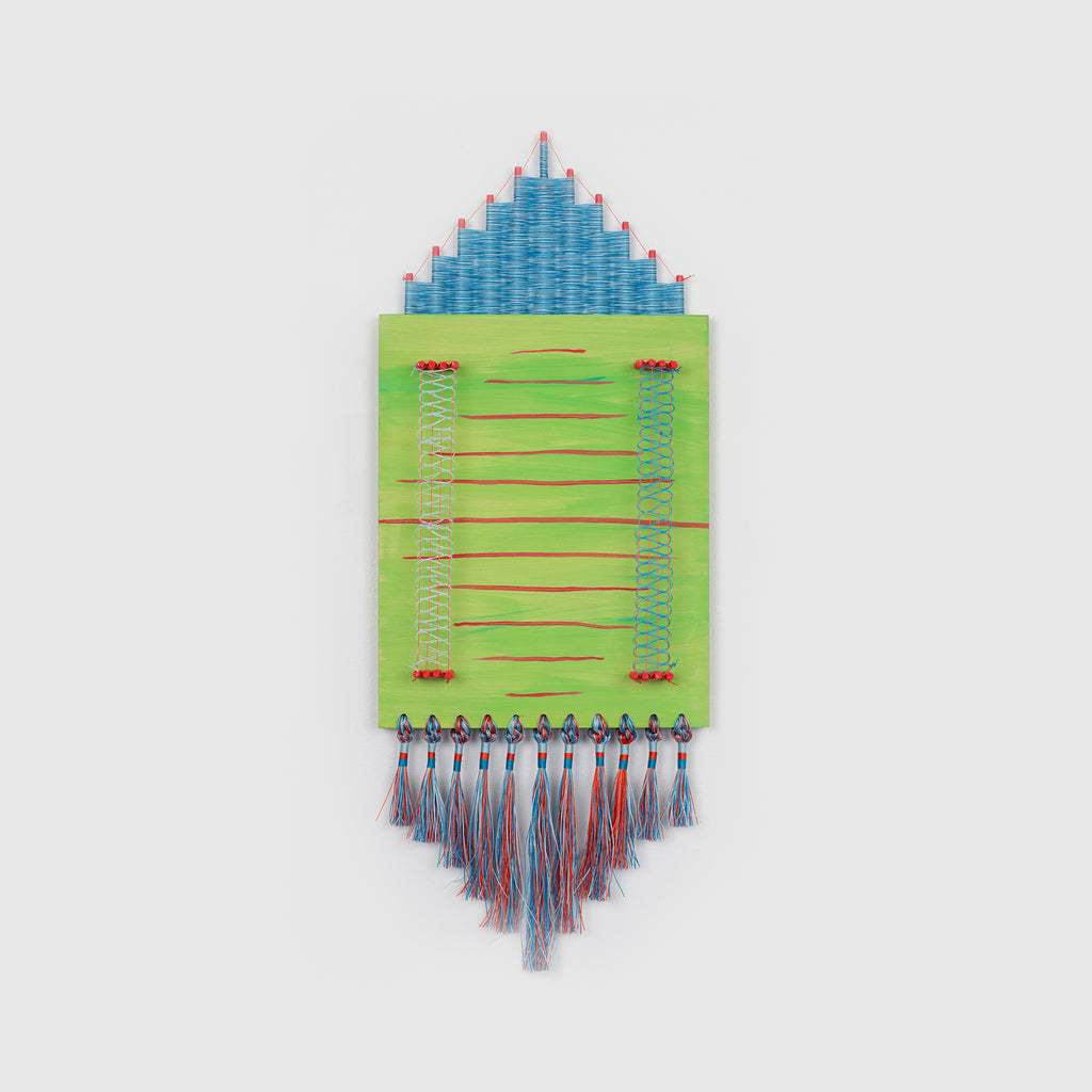 The artwork 'The Field' by Amber Heaton features a geometric composition with a blue triangular peak above a lime green rectangular base. Red horizontal lines cross the green section, accented by blue decorative stitching. Multicolored tassels in blue, red, and gray hang from the bottom, creating a dynamic textile-like appearance. Acrylic on wood with cord embellishments.