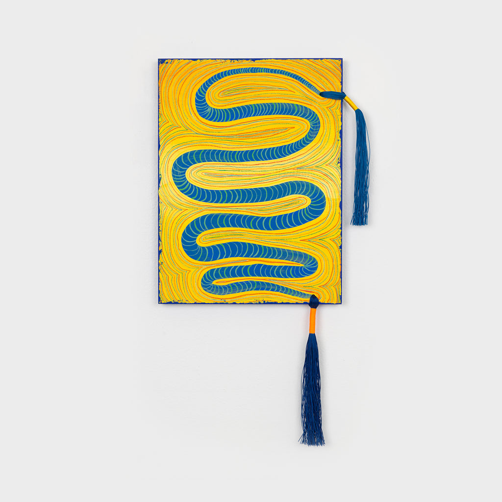 The artwork 'The River' by Amber Heaton features a bold serpentine pattern in vibrant royal blue winding across a bright yellow background. The acrylic painting on wood showcases rhythmic, flowing lines with dynamic movement, complemented by decorative navy blue and orange tassels hanging from opposite corners. The contemporary abstract design measures 22 by 14 inches.