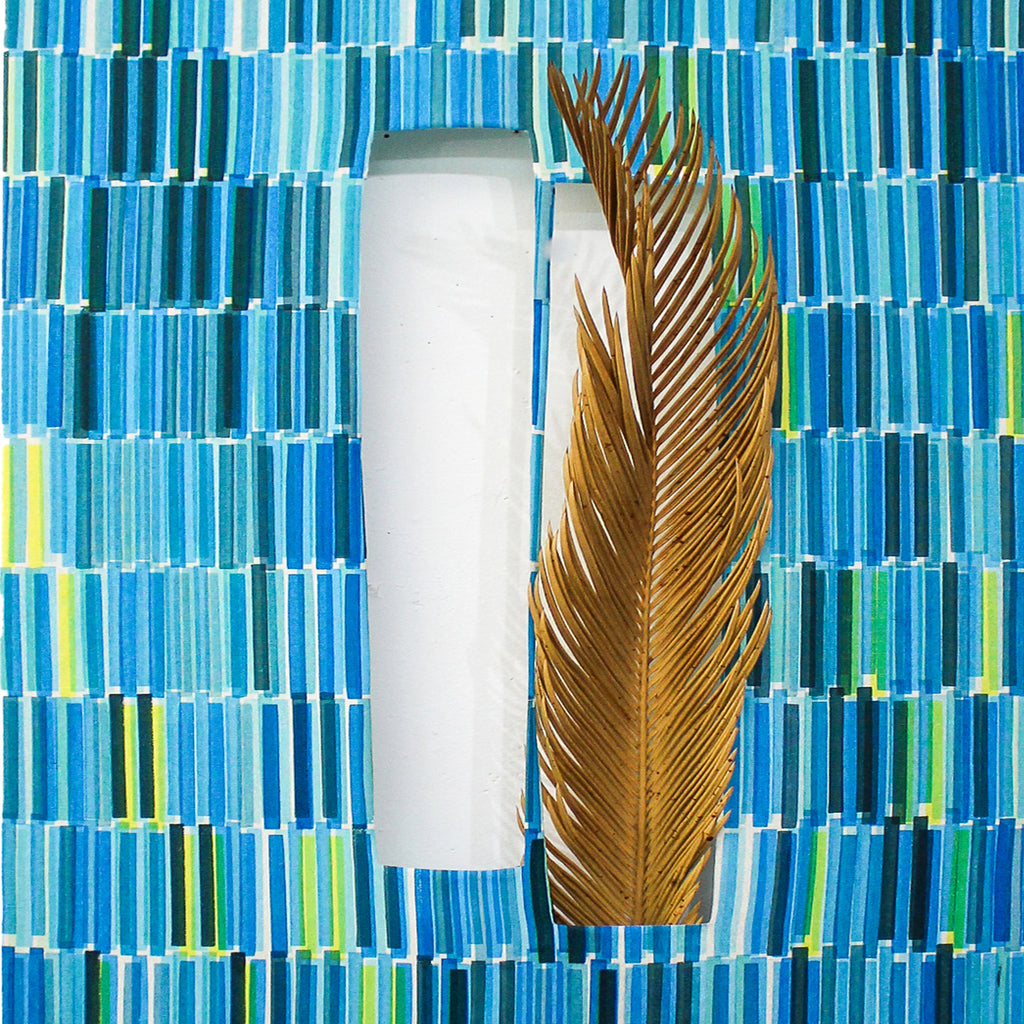 The artwork 'Composite 21' by Molly Koehn features a vertical white cylindrical form alongside a dried brown palm frond, set against a geometric background of mosaic-like blue tiles. The screen-printed pattern on raw silk creates a rhythmic arrangement of turquoise and aqua rectangles with occasional yellow accents. 40x18 inches handcrafted artwork by Molly Koehn.