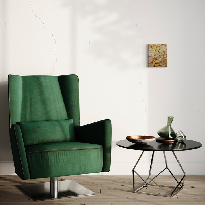 Déflorées Origins Tulip 06' artwork displayed in a modern interior setting, featuring emerald green velvet armchair and round black side table. Wall-mounted floral artwork with warm golden tones, preserved petals on canvas. Mixed media composition by Valerie Hallier.