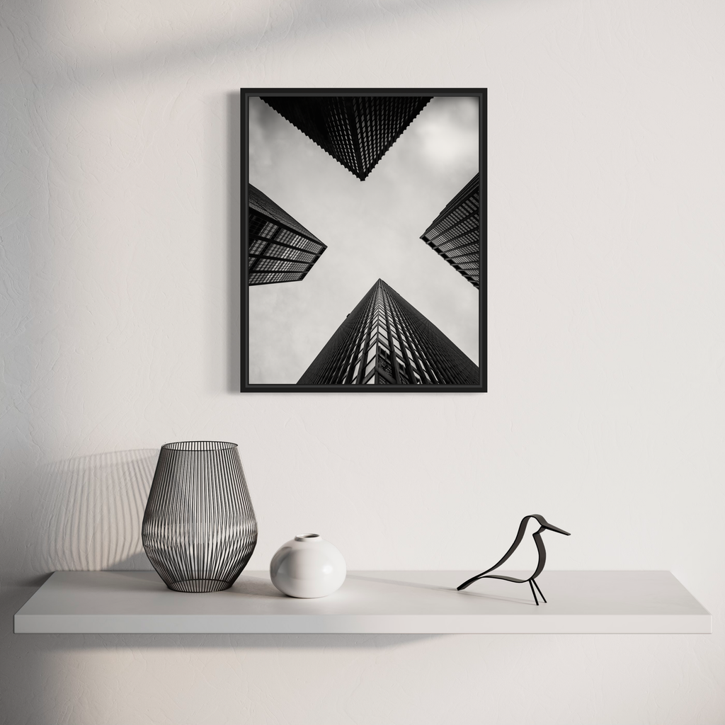 The artwork '4 Corners' by Dennis Maida features a striking black and white architectural photograph of four skyscrapers converging to form an X shape against a bright sky, captured from a dramatic upward perspective. The monochromatic composition emphasizes geometric patterns and angular lines of modern urban architecture.