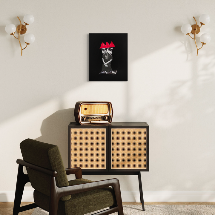 The artwork 'His Eyes Looking At You' by Courtney Minor features a black and white collage on canvas mounted in a minimalist interior setting, displayed above a vintage-style cabinet with cane webbing. The artwork contrasts with a cream wall, flanked by brass sconces with globe lights. A mid-century modern olive green armchair completes the retro-inspired scene.