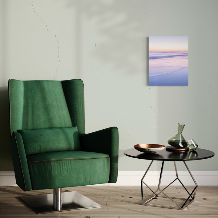 Portrait du point du jour #2 by Fabienne Sowa-Dobkowski features a serene minimalist photograph displayed in a modern interior setting, mounted against a light gray wall above a black round side table. The 20x16 inch meta print captures soft pastel hues of dawn in purple and blue tones, complemented by an emerald green velvet armchair in the foreground.