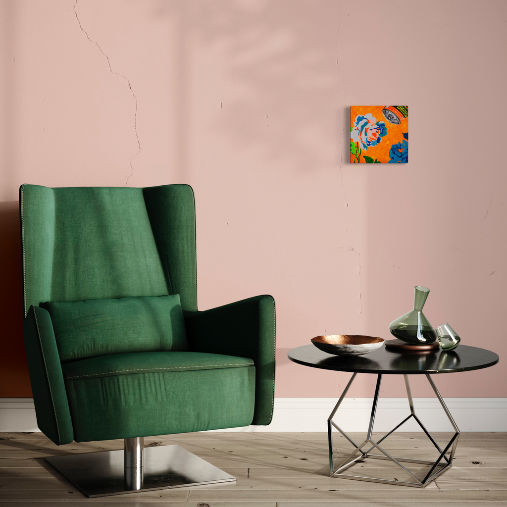 The artwork 'Sense Sustinance' by Mary Younkin features a modern interior setting with a plush emerald green velvet wingback chair, positioned beside a contemporary black round side table with geometric metal base. A small vibrant artwork with orange and blue tones hangs on the soft pink wall, creating an elegant contrast against the minimalist decor. 10x10 inch acrylic on wood panel.