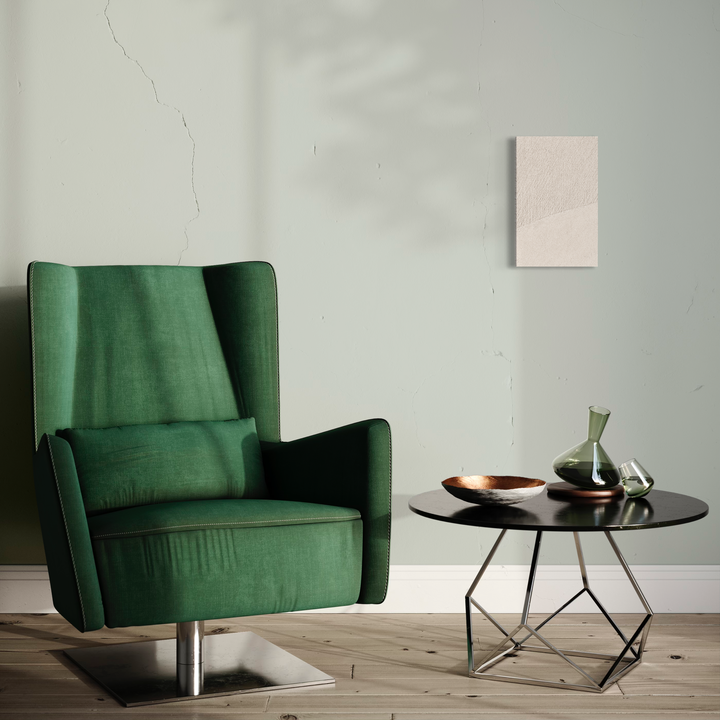 The artwork 'Serenity #1' by Fabienne Sowa-Dobkowski features a minimalist interior setting with an emerald green velvet wingback chair, positioned beside a modern round black side table. The table displays decorative glass vessels and a copper bowl against a soft gray wall backdrop, creating a contemporary yet tranquil composition.
