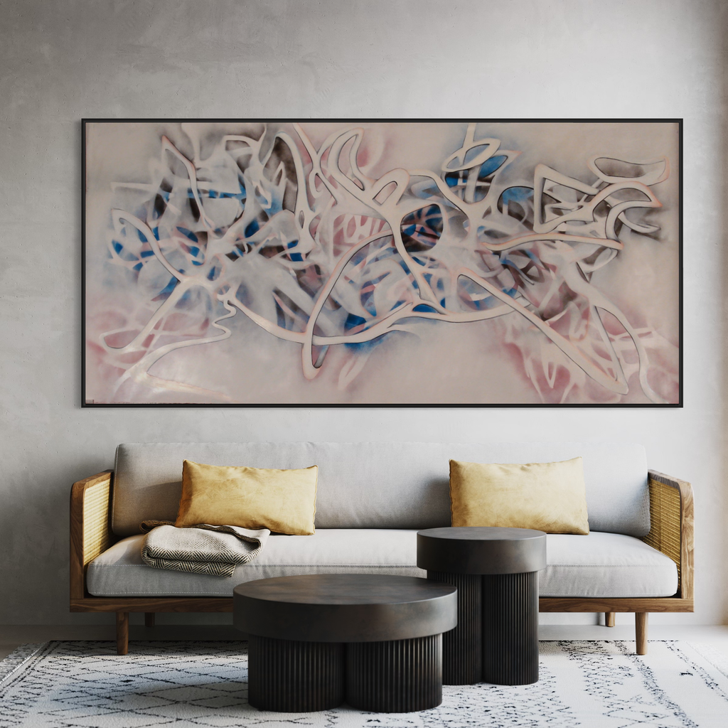 The artwork 'Big Sky' by Megan Olson features flowing abstract forms in soft pink and white with accents of vibrant blue, created using spray paint and oil on paper. The composition suggests ethereal movement with interweaving curved lines and translucent layers, mounted in a sleek black frame above a modern sofa setting.