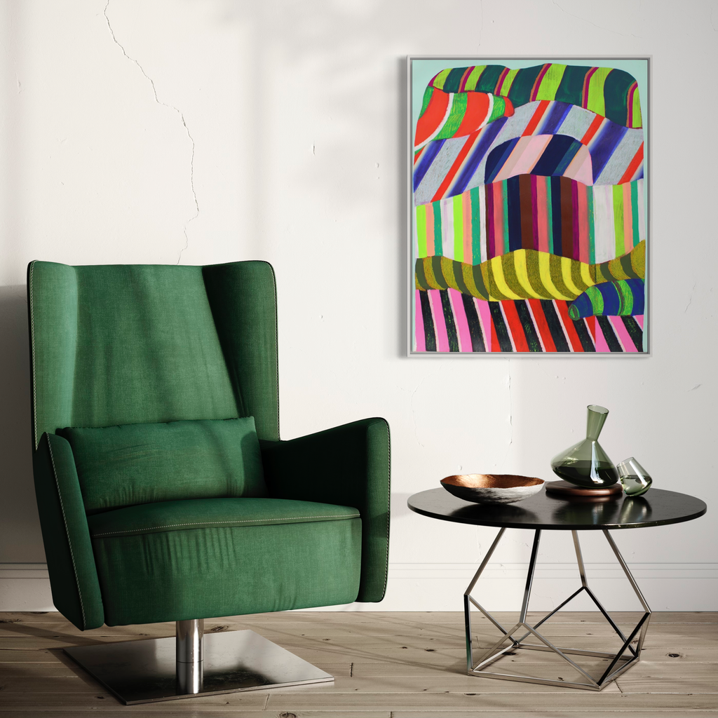 The artwork 'Erratic' by Natalie Lanese features vibrant geometric stripes in undulating patterns, combining neon greens, pinks, blues, and purples. The abstract composition creates a dynamic optical illusion through curved parallel lines and bold color blocks, displayed above an emerald green armchair and modern side table.