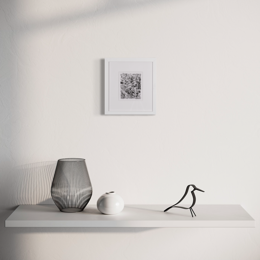 The artwork 'Pathways (2)' by Diana Naccarato features a minimalist display with a framed black and white abstract charcoal drawing on a white wall, accompanied by contemporary decor including a ribbed gray wire vase, white ceramic vessel, and decorative black bird figurine arranged on a floating gray shelf.