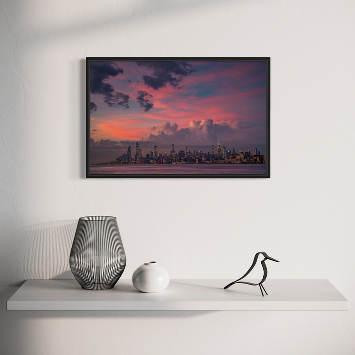 The artwork 'Pink Apple' by Dennis Maida captures a dramatic cityscape at sunset, featuring a vibrant pink and purple sky with billowing clouds hovering over an urban skyline. The photographic composition showcases illuminated skyscrapers silhouetted against the twilight horizon, creating a stunning contrast between modern architecture and natural beauty.