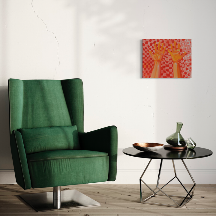 The artwork 'Pizza Hands' by Chelsie Sunde features two upward-reaching hands against a vibrant checkered pattern background in coral and pink tones. The oil painting on canvas creates a playful, pop art aesthetic, displayed above an emerald green armchair in a modern interior setting with a round side table and decorative vases. - Chelsie Sunde