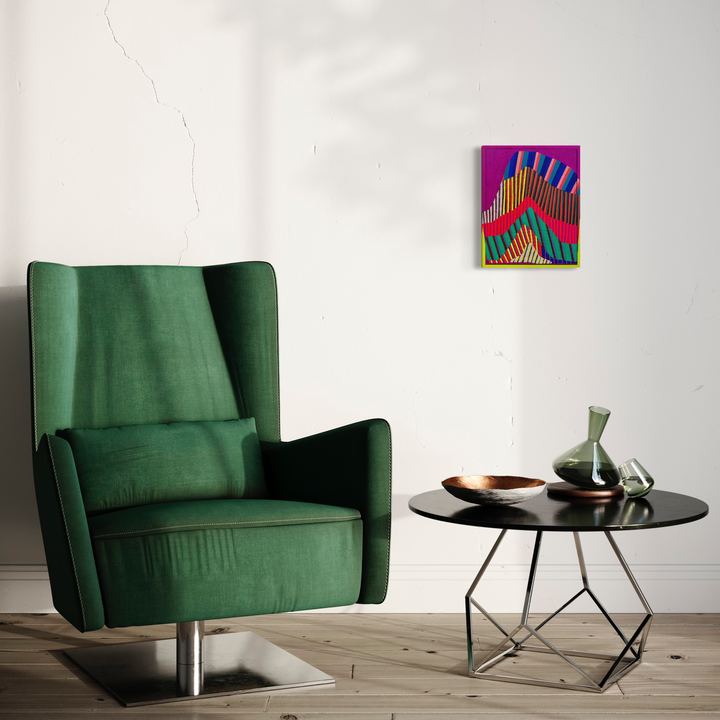 The artwork 'Slow Uplift' by Natalie Lanese features vibrant geometric patterns in magenta, orange, and teal, displayed on a white wall above a modern emerald green velvet armchair and round black side table. The abstract composition shows dynamic zigzag forms creating a sense of upward movement, painted using Flashe, DayGlo and oil on paper in a found frame.