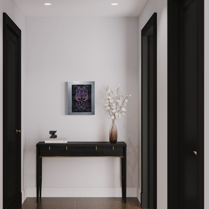 The artwork 'The Light & Dark Within Me - Dark Neon Edition' by IvIvI features a glowing purple feline design on black glitter acrylic, displayed in a modern hallway setting above a sleek black console table. The artwork's silver border complements the contemporary interior with white walls and dark doors. Archival ink on gessobord, 20x16 inches. By IvIvI.