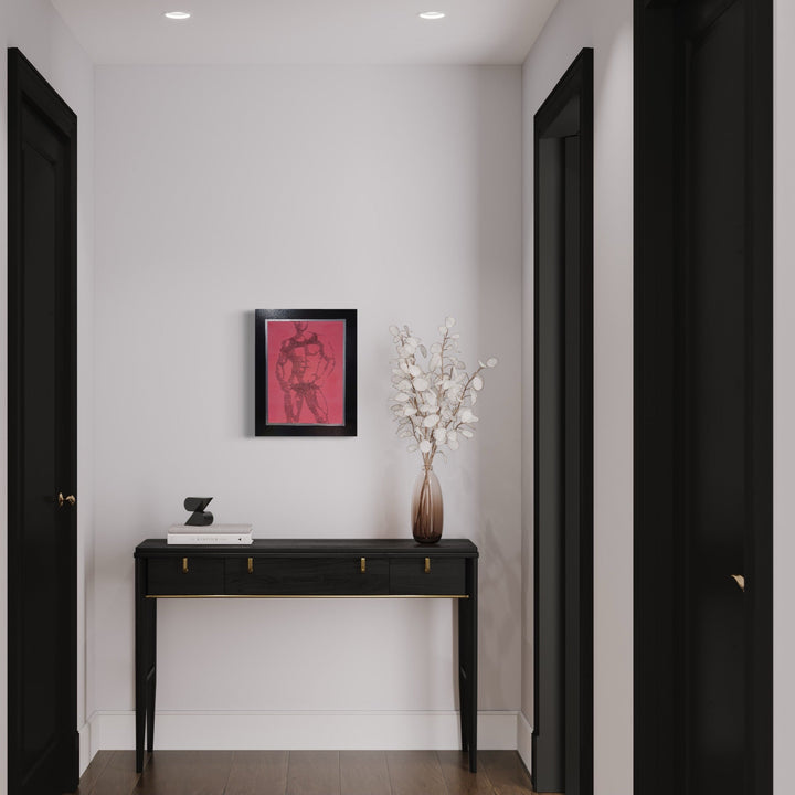 The artwork 'Pose For Me - Neon Pink Edition' by IvIvI features a minimalist line drawing in archival ink on glow-in-the-dark pink acrylic, displayed in a black frame on a white wall above a modern black console table. The piece is bordered with hand-painted black and silver details, creating a striking contrast against the crisp white interior space.