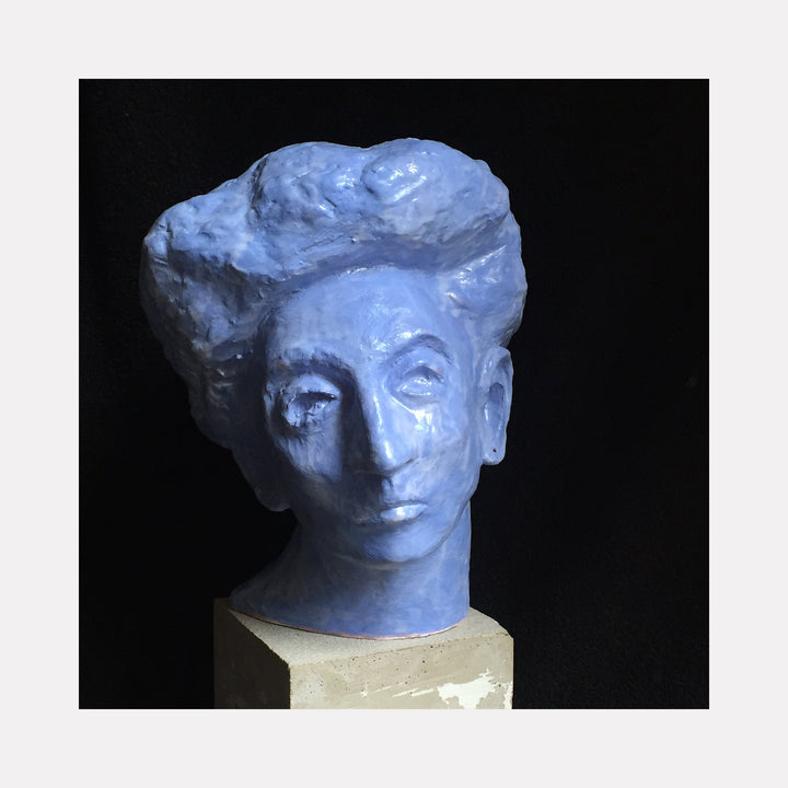 The artwork 'Blue Queen' by Mark LaRiviere features a sculptural head rendered in vibrant cobalt blue glazed ceramic. The piece showcases elegant curves and textural details, mounted on a neutral-toned metal base. The sculptural work exhibits a contemporary artistic style with classical portrait influences. 10x9x9.5 inches. By Mark LaRiviere.