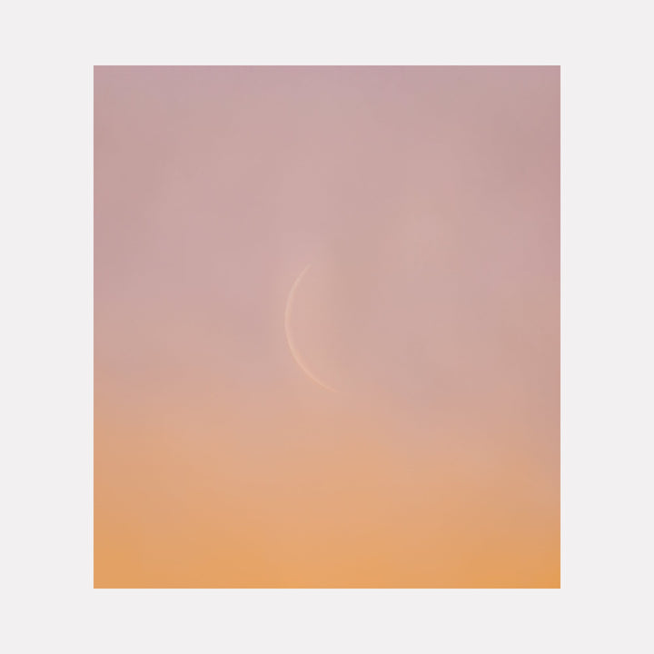 The artwork 'C Moon' by Dennis Maida captures a minimalist photographic composition featuring a subtle crescent moon form against a dreamy gradient background, transitioning from soft mauve pink to warm peach orange. The ethereal atmosphere creates a contemplative mood through its delicate color palette and celestial imagery.