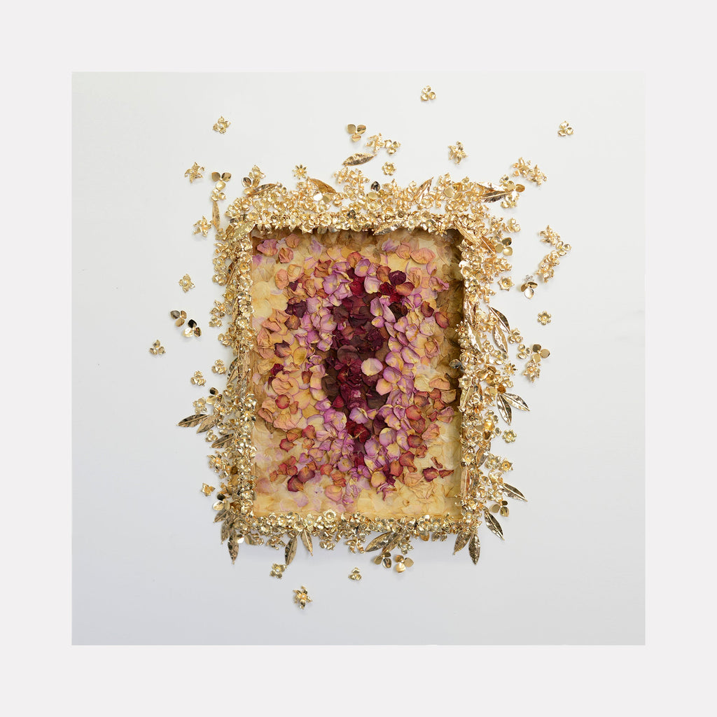The artwork 'Défloré(e)s Story #4' by Valerie Hallier features pressed rose petals arranged in a deep concentric pattern, transitioning from dark burgundy at the center to soft pink edges, framed by an intricate border of gold-toned floral elements on a white panel. The mixed media piece combines natural and metallic materials creating a textured, dimensional effect.