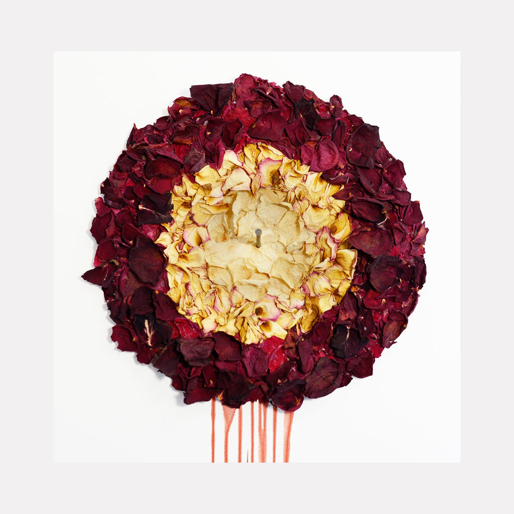 The artwork 'Deflore(e)s Story #5' by Valerie Hallier features a circular composition of pressed rose petals arranged in a dramatic gradient from deep burgundy outer ring to pale golden center, with striking red liquid trails beneath, mounted against white background. Created with pressed flowers and vampire blood, 69x16 inches.