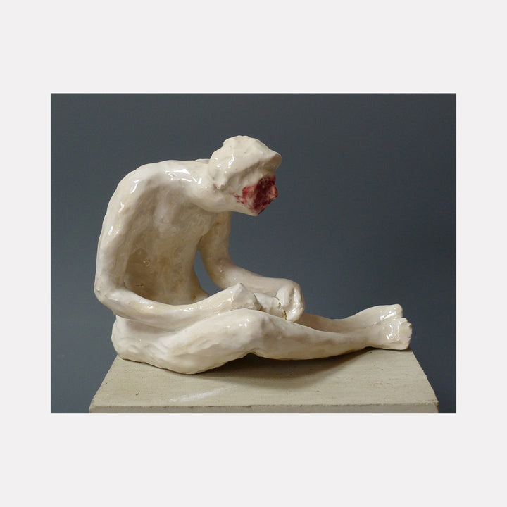The artwork 'Embarrassed' by Mark LaRiviere features a glazed ceramic sculpture of a figure in white, seated in a curled position suggesting vulnerability. The sculpture's smooth, glossy surface creates a striking contrast against the dark background, showcasing fluid lines and organic forms in this intimate portrayal of human emotion.