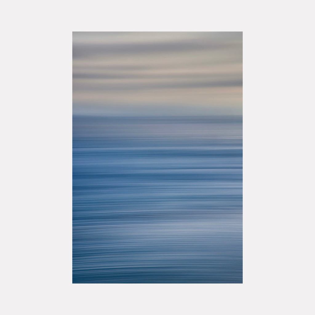 The artwork 'Malibu' by Neil Shapiro features a serene abstract seascape with horizontal motion blur, transitioning from deep ocean blue at the bottom to misty beige tones at the top. The smooth gradient effect creates a tranquil, minimalist composition that captures the essence of coastal waters meeting cloudy skies.