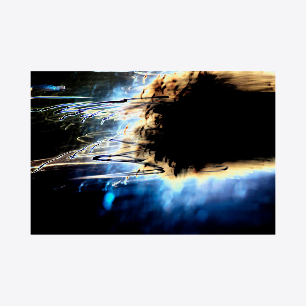 The artwork 'Particle Physics 01' by Chunbum Park features abstract light trails creating dynamic movement across a dark background. Luminous streaks of electric blue and golden yellow interweave through deep shadows, suggesting cosmic energy or subatomic particles in motion. The photograph captures fluid, ethereal textures with dramatic contrast between light and darkness. By Chunbum Park.