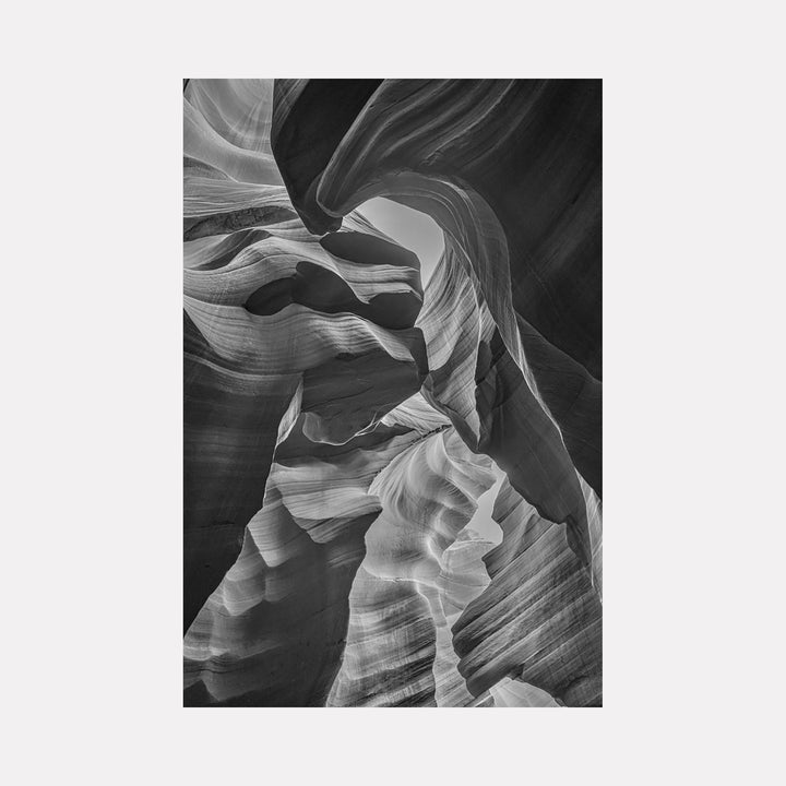 The artwork 'Slot Canyon In B & W' by Neil Shapiro captures dramatic sweeping curves of eroded sandstone in striking monochrome. Smooth, undulating rock formations create flowing lines and abstract patterns, with deep shadows and bright highlights emphasizing the canyon's natural sculptural qualities. Metal print showcases intricate textures and layered striations of the weathered rock walls.