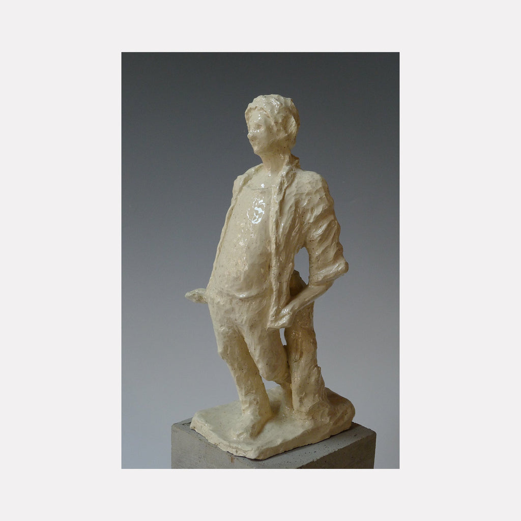 The artwork 'Standing Man Walking' by Mark LaRiviere features a glazed ceramic sculpture depicting a figure in a casual stance, with one hand resting on hip. The creamy white finish creates a luminous surface texture, while the dynamic pose suggests movement and contemplation. The sculptural form showcases detailed folds in clothing and a refined artistic style.