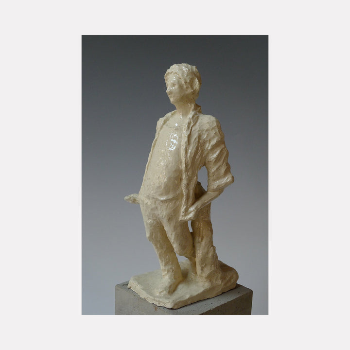 The artwork 'Standing Man Walking' by Mark LaRiviere features a glazed ceramic sculpture depicting a figure in a casual stance, with one hand resting on hip. The creamy white finish creates a luminous surface texture, while the dynamic pose suggests movement and contemplation. The sculptural form showcases detailed folds in clothing and a refined artistic style.