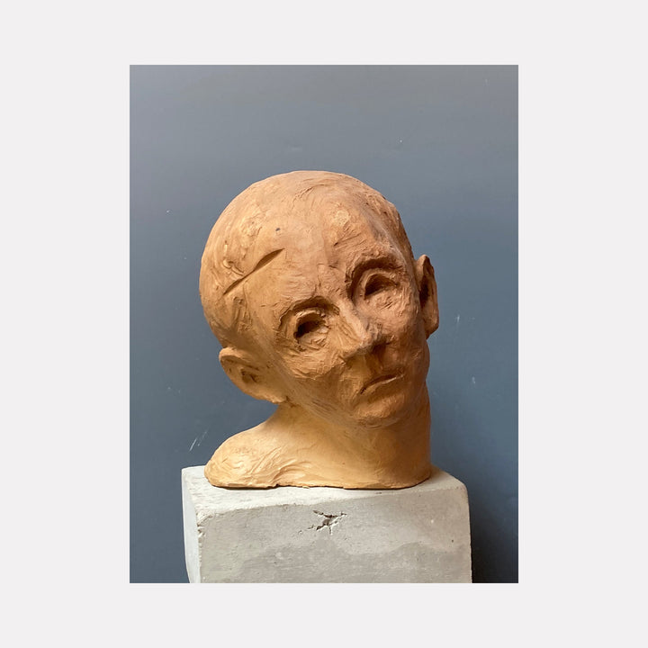 The artwork 'Young Boy' by Mark LaRiviere features a sculptural ceramic head with expressive features, tilted upward at an angle. The milk-glazed ceramic surface exhibits a warm terracotta hue, capturing fine textural details in a naturalistic style. The sculpture rests on a white square base against a gray background.