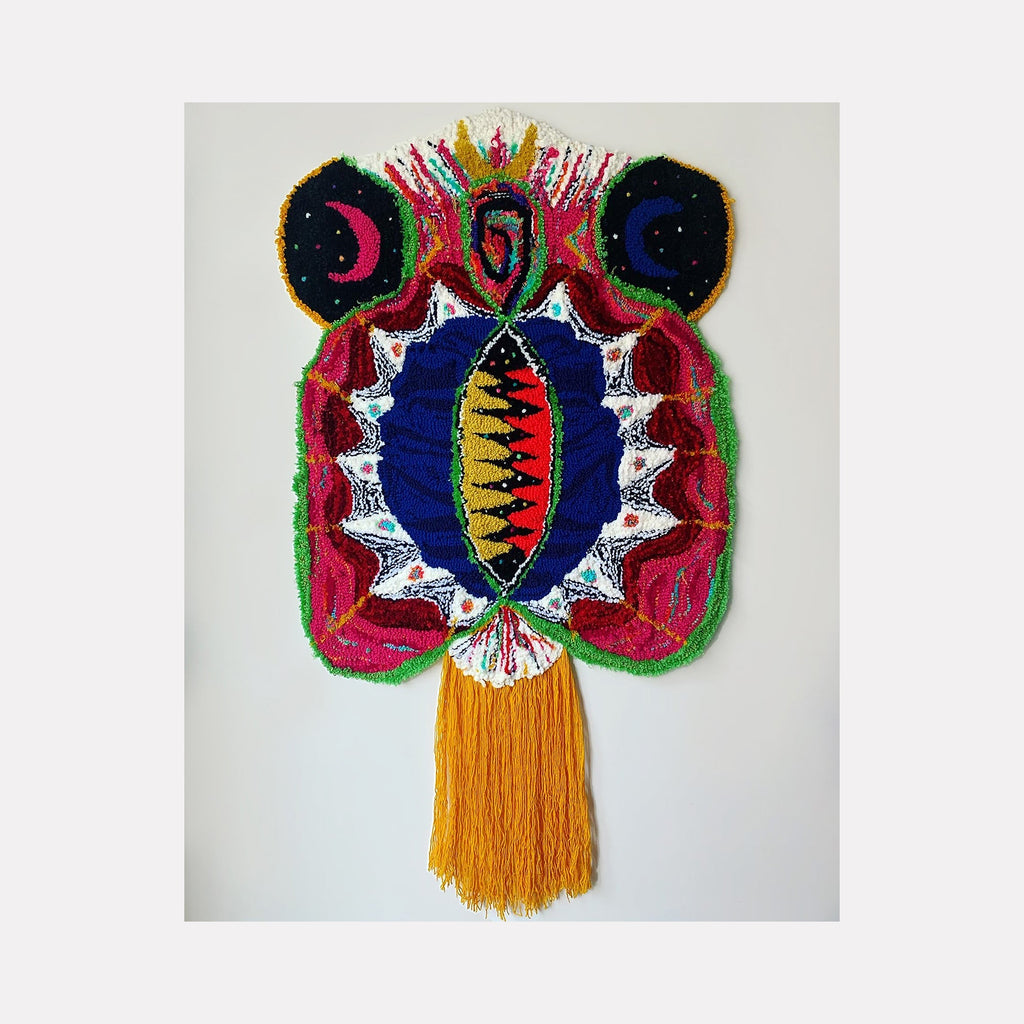 The artwork 'histerica #4' by Ana Maria Farina features a vibrant fiber art piece with symmetrical circular motifs in deep blue, hot pink, and green. A central almond-shaped design adorned with white lace-like edges contains yellow and black patterns. Golden fringe tassels cascade from the bottom, while crescent moon shapes accent the top corners. Created using upcycled fibers on monk's cloth.