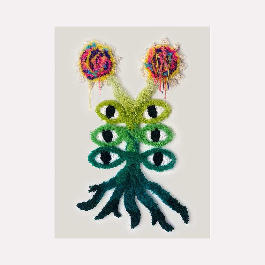 The artwork 'Selva' by Ana Maria Farina features a surreal creature with six vertically-aligned eyes in gradating shades of green, crowned by two vibrant abstract flowers in explosive bursts of pink, purple, yellow, and orange. Created with upcycled fibers on linen, the piece displays a mystical, forest-inspired character emerging from emerald tentacle-like roots.