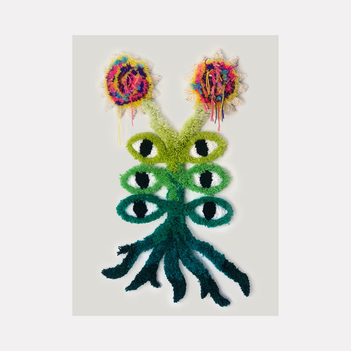The artwork 'Selva' by Ana Maria Farina features a surreal creature with six vertically-aligned eyes in gradating shades of green, crowned by two vibrant abstract flowers in explosive bursts of pink, purple, yellow, and orange. Created with upcycled fibers on linen, the piece displays a mystical, forest-inspired character emerging from emerald tentacle-like roots.