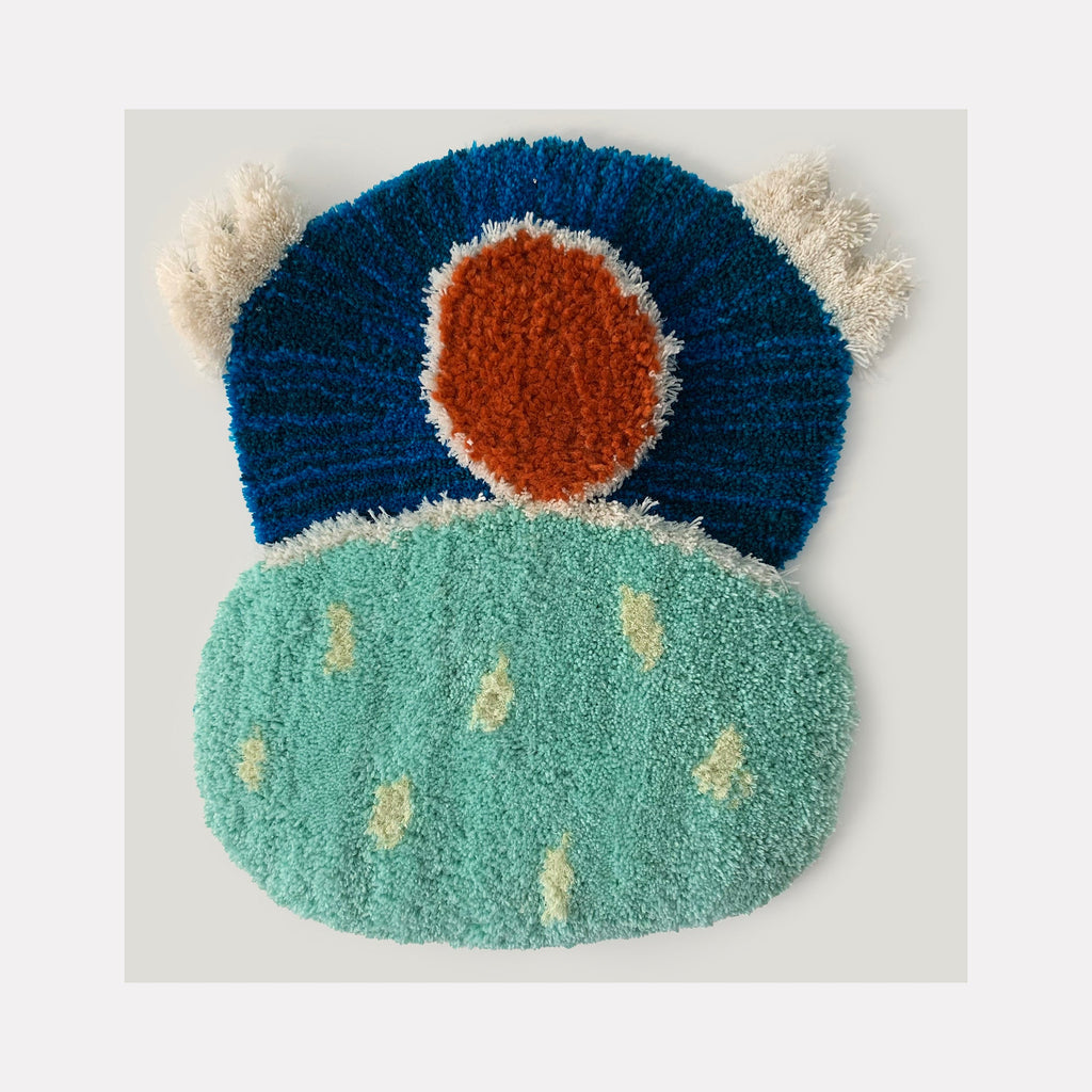The artwork 'Soothe' by Ana Maria Farina features a textural fiber composition with a deep blue arc crowned by a rust-orange circle, floating above a mint green oval base dotted with cream accents. Created from upcycled fibers on linen, the piece showcases contrasting textures and colors in an abstract, whimsical design measuring 23.5 x 21 inches.