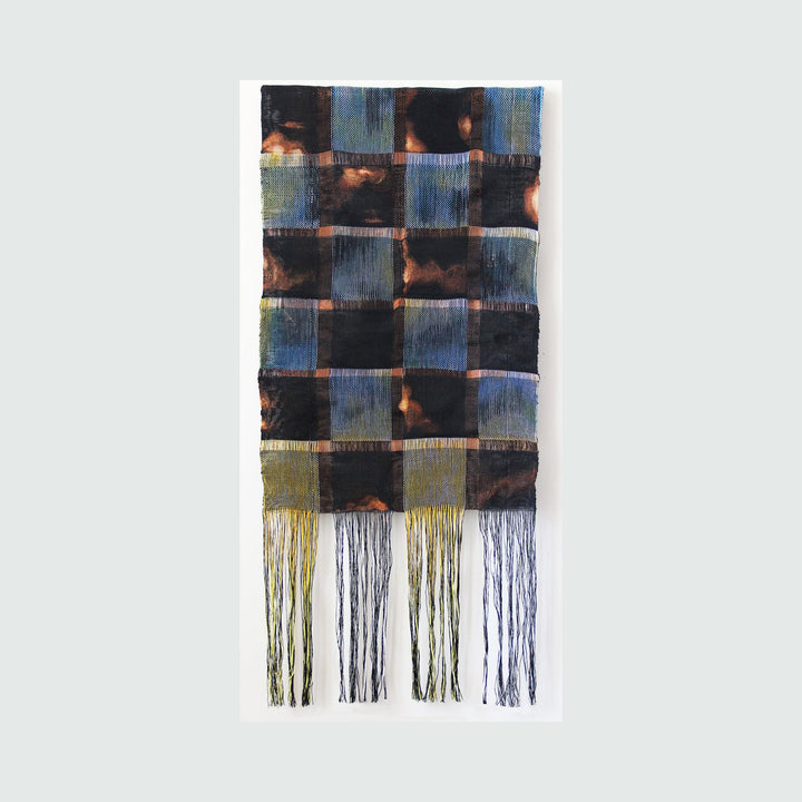The artwork 'Lights Will Not Go Out' by Kathie Halfin features a woven textile composition of checkered squares in deep indigo blue and burnt copper tones. The handcrafted piece combines linen and copper wire in an alternating pattern, with long, delicate cotton threads cascading from the bottom, creating a dramatic dripping effect. The 45-inch textile artwork showcases a unique interplay of metallic and natural materials.