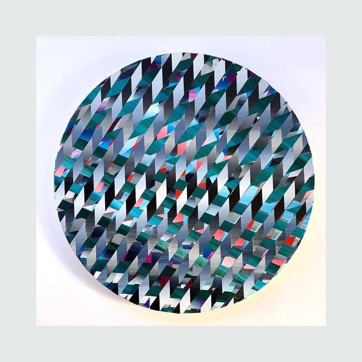 The artwork 'Push Through' by Elyce Abrams features a dynamic geometric pattern of interlocking chevrons in metallic silver, teal, and turquoise, with subtle pops of red and pink, painted in acrylic on a 12-inch round wood panel. The repeating angular shapes create a mesmerizing optical effect, suggesting movement and depth across the circular composition.