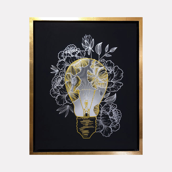 The artwork 'Inspire Me - Gold & Silver Edition' by IvIvI features a lightbulb illustration in metallic gold and silver on black background, surrounded by delicate peony blooms and leaves. The design combines modern minimalism with floral elegance, rendered in archival ink on acrylic-painted Gessobord with gold frame.