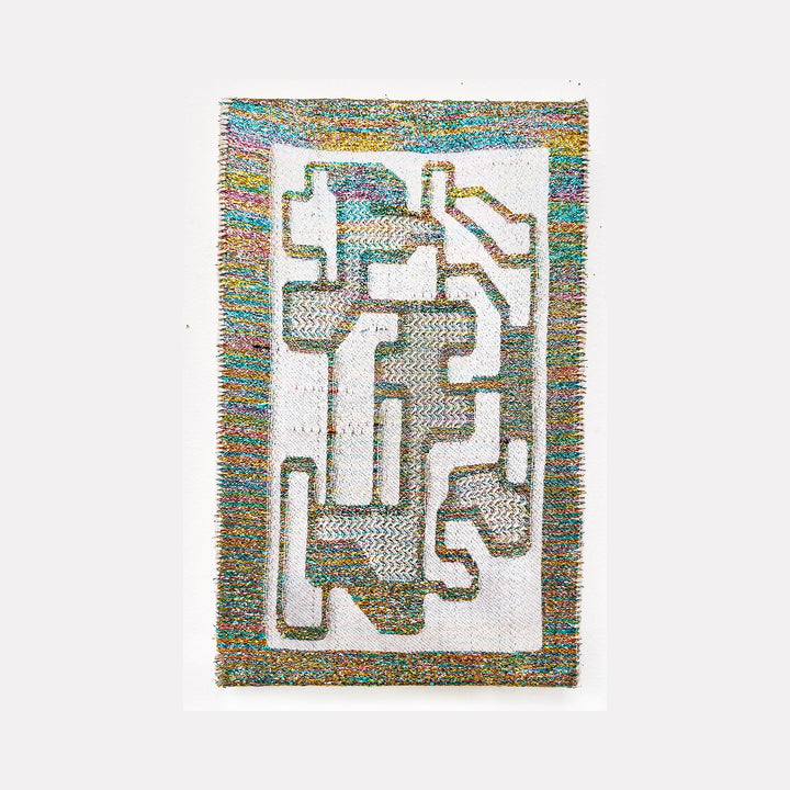The artwork 'Divine Blueprint' features an abstract geometric composition of interlocking angular shapes woven in iridescent metallic and cotton yarn. The design resembles a maze-like pattern with white negative spaces, bordered by a shimmering multicolored frame that transitions through turquoise, gold, and purple hues. Handwoven textile art by Robin Kang.