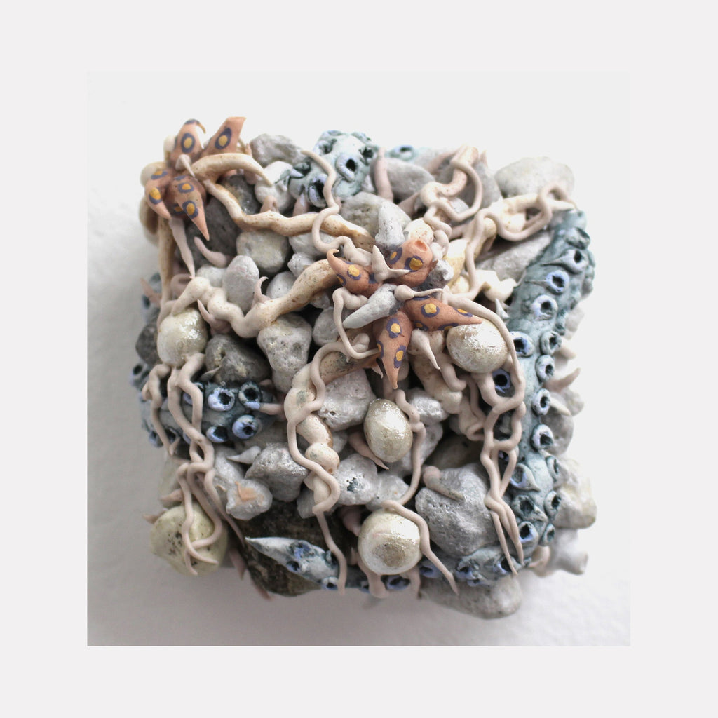 The artwork 'Pelagic' by Seren Morey features an intricate textural composition of intertwining organic forms in pale blue, beige, and coral tones. The sculptural surface combines sinuous curves and spherical elements with rough, pumice-textured areas, creating a marine-inspired abstract relief that appears to flow and undulate across the square panel, rendered in ultralight acrylic and mixed media.
