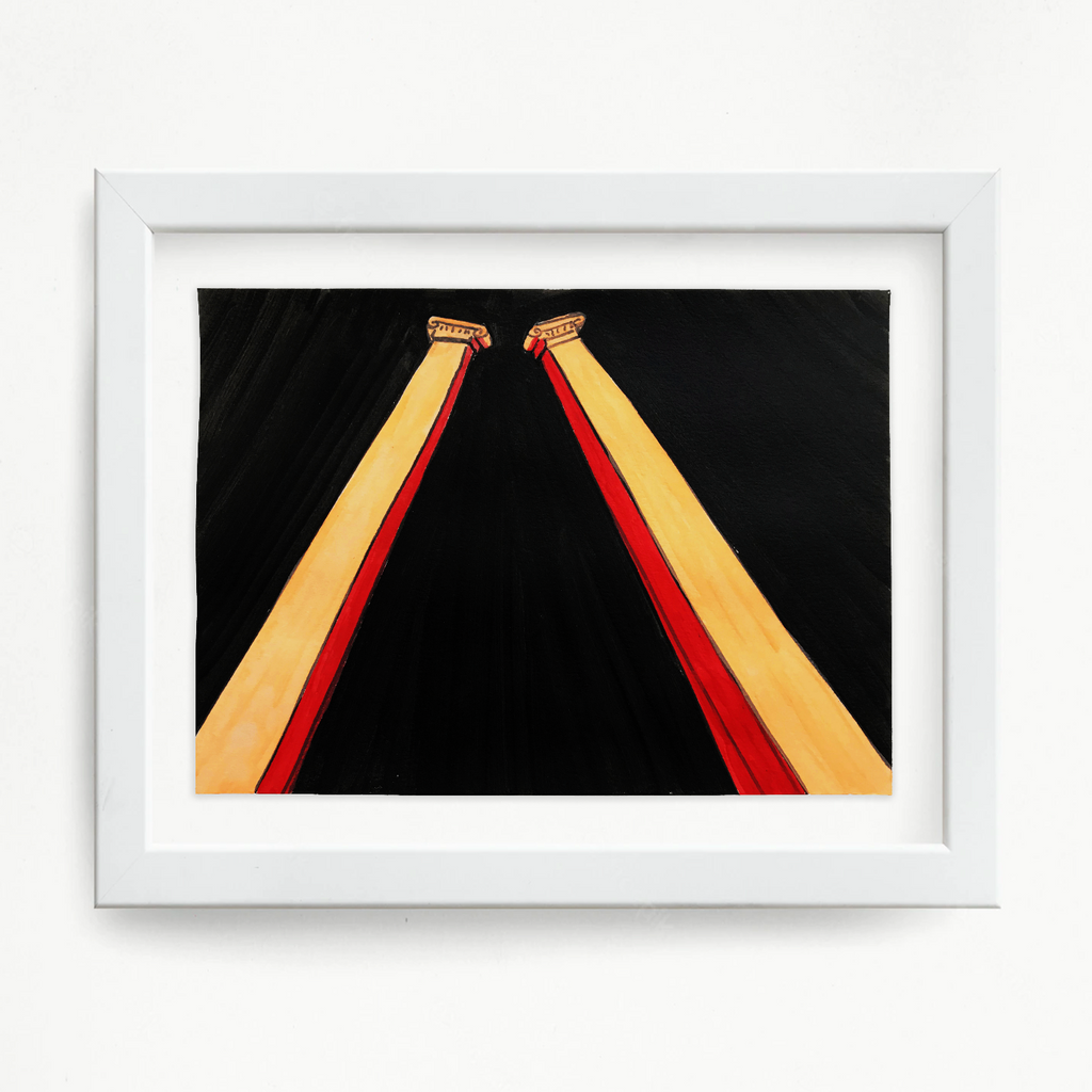 The artwork 'Columns (orange)' by Til Will features two striking diagonal columns in vibrant orange and red tones against a deep black background. The columns create a dramatic V-shape composition, with ornate capitals at the top. The mixed media piece combines acrylic and ink on watercolor paper, presented in a clean white frame.
