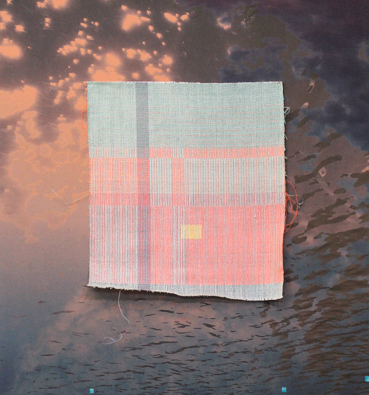 The artwork 'something about the weather 4' by Molly Koehn features a handwoven square composition blending soft pink and pale blue tones. A delicate grid pattern emerges through stainless steel and textile materials, with a subtle yellow accent. Set against a dramatic sunset-like background, the piece showcases minimalist geometric design through mixed media craftsmanship.